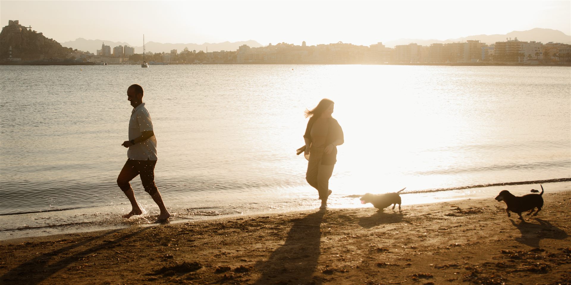 Pareja paseando con sus perros al atardecer en la playa de Águilas — Luarna Studio